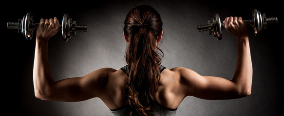 Atractive fit woman works out with dumbbells as a fitness conceptual over dark background - 487073986