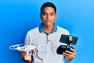 Young handsome hispanic man using drone holding remote control relaxed with serious expression on face. simple and natural looking at the camera.