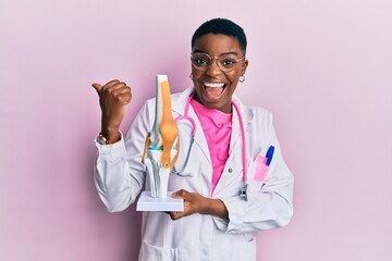 Young african american doctor woman holding anatomical model of knee joint pointing thumb up to the...