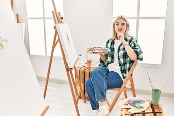 Young artist woman painting on canvas at art studio thinking worried about a question, concerned...