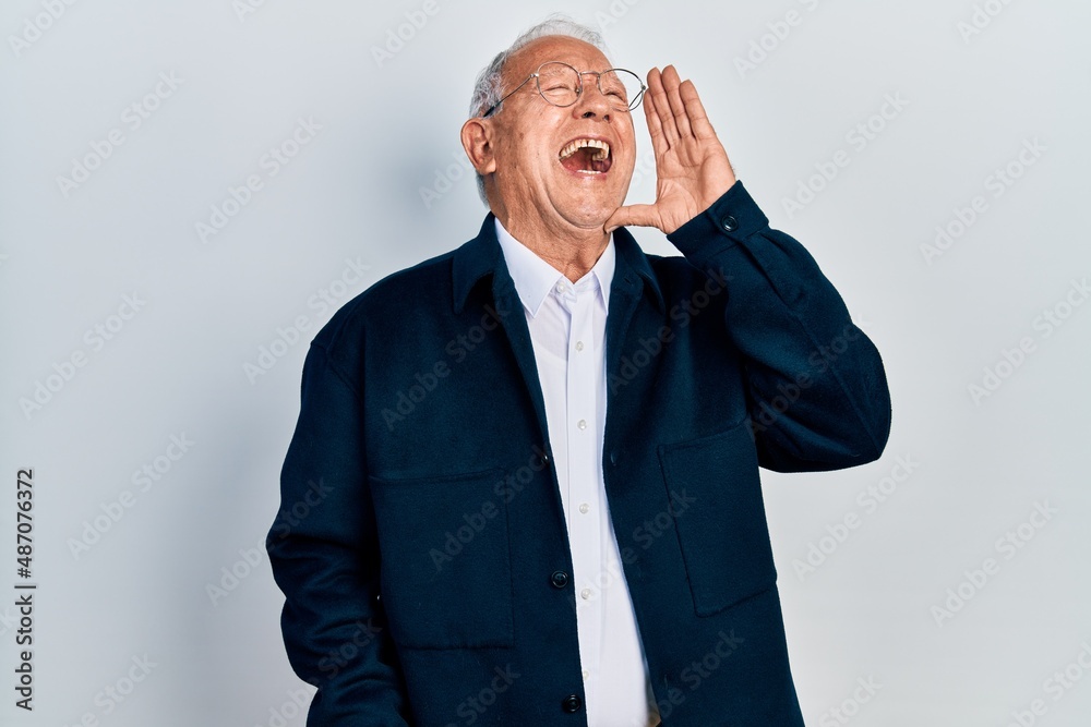 Wall mural Senior man with grey hair wearing casual style and glasses shouting and screaming loud to side with hand on mouth. communication concept.