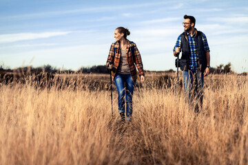 Couple with backpacks hiking together in nature on autumn day.