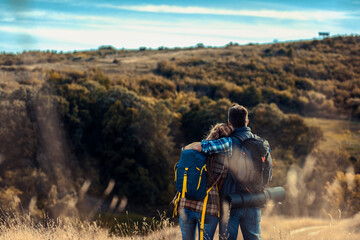 Fototapeta na wymiar Rear view of couple with backpacks hiking together in nature on autumn day.