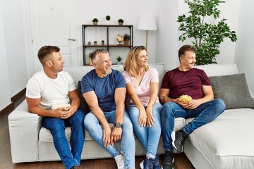 Group of middle age people sitting on the sofa at home looking to side, relax profile pose with natural face and confident smile.