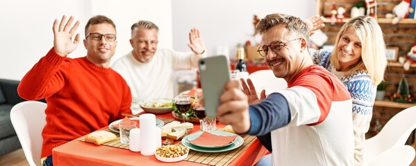 Group of middle age friends smiling happy having christmas dinner and video call by the smartphone at home.
