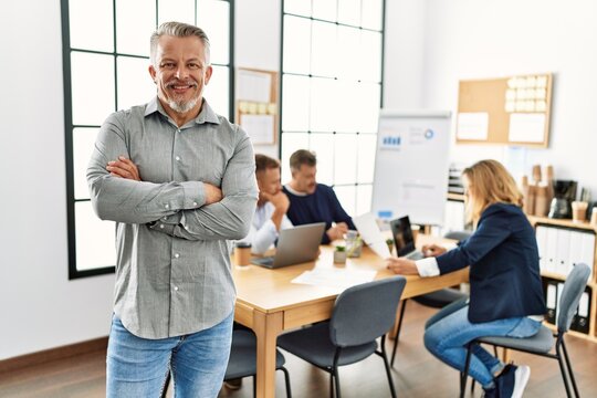 Middle age caucasian businessman smiling happy standing with arms crossed gesture at the office during business meeting.