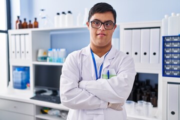 Down syndrome man wearing scientist uniform standing with arms crossed gesture at laboratory