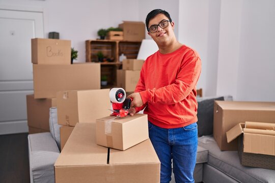 Down syndrome man smiling confident packing cardboard box at new home