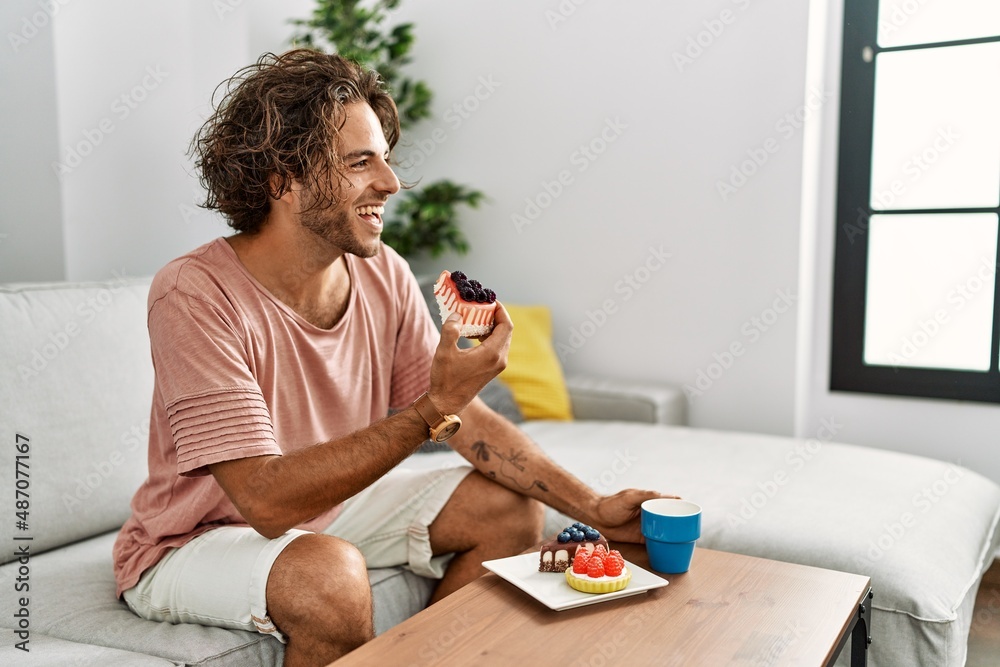 Canvas Prints Young hispanic man having breakfast sitting on the sofa at home.