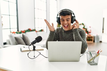 Handsome hispanic man recording podcast celebrating victory with happy smile and winner expression with raised hands