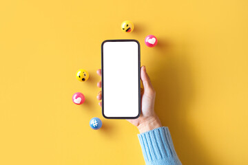 Hand of woman holding blank mobile phone with love, like, comment, hashtag button on yellow background. Social media marketing concept - obrazy, fototapety, plakaty