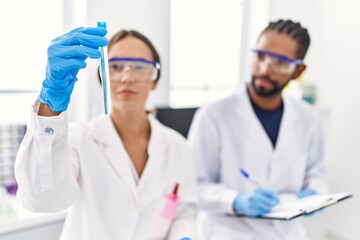 Man and woman scientist partners holding test tube and writing on clipboard at laboratory
