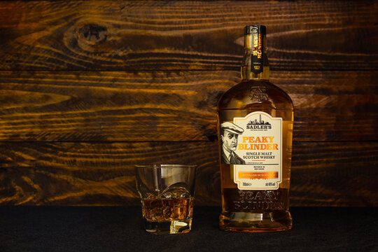 Bottle of Sadler's Peaky Blinder Scotch Whisky and a glass with ice on a dark wooden background. The Peaky Blinder Bourbon reflects the true American spirit.