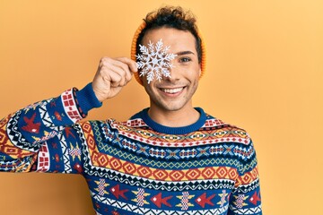 Young handsome man holding snowflake wearing winter sweater looking positive and happy standing and...