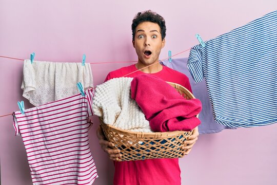 Handsome hispanic man doing laundry holding wicker basket afraid and shocked with surprise and amazed expression, fear and excited face.