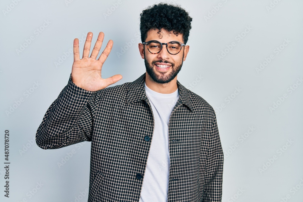 Sticker young arab man with beard wearing glasses showing and pointing up with fingers number five while smi