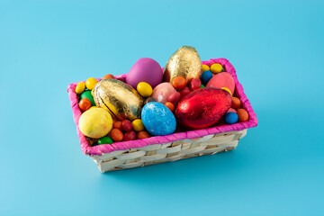 Colorful chocolate Easter eggs in a basket on blue background