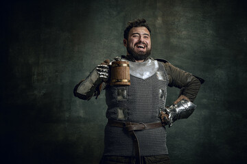 Happy medieval warrior or knight with dirty wounded face holding big mug of beer isolated over dark...