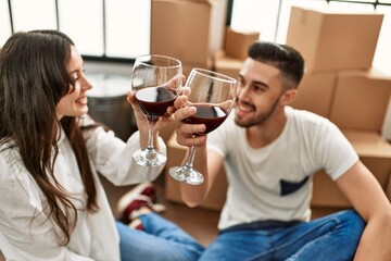Young hispanic couple smiling happy toasting with red wine at new home.