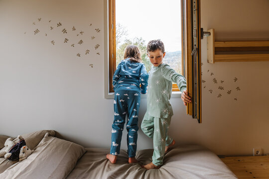 Siblings in pajamas looking out window