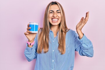 Beautiful hispanic woman holding earwax cotton removers celebrating victory with happy smile and...