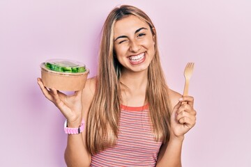 Beautiful hispanic woman eating salad winking looking at the camera with sexy expression, cheerful...