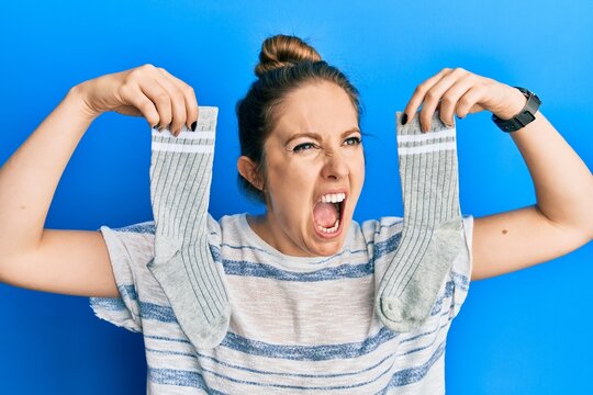 Young blonde woman holding socks angry and mad screaming frustrated and furious, shouting with anger. rage and aggressive concept.
