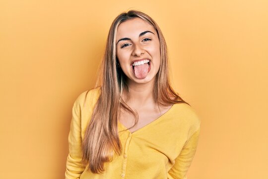 Beautiful hispanic woman wearing casual yellow sweater sticking tongue out happy with funny expression. emotion concept.