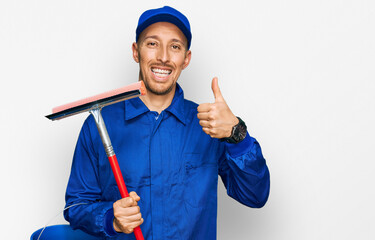 Bald man with beard wearing glass cleaner uniform and squeegee smiling happy and positive, thumb up...