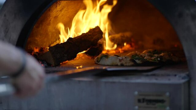Brick oven pizza being placed in oven slow