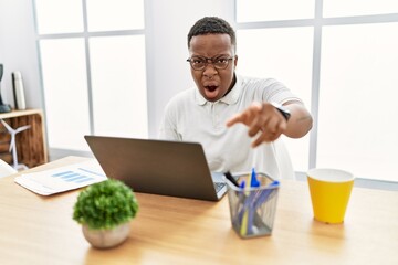 Young african man working at the office using computer laptop pointing displeased and frustrated to the camera, angry and furious with you