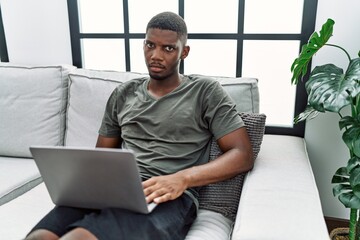 Young african american man using laptop at home sitting on the sofa depressed and worry for distress, crying angry and afraid. sad expression.