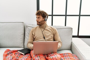 Young handsome man with beard wearing operator headset working from home looking to side, relax...