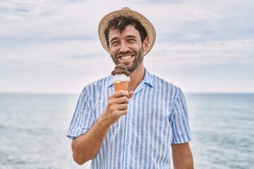 Young hispanic man smiling happy eating ice cream at the beach.