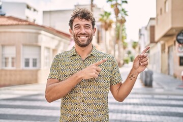 Young hispanic man standing at the street smiling and looking at the camera pointing with two hands and fingers to the side. © Krakenimages.com