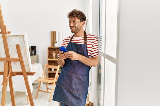 Young hispanic man smiling confident using smartphone at art studio