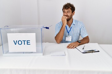 Young handsome man at political election sitting by ballot looking stressed and nervous with hands...