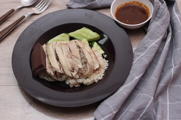 Hainanese chicken rice served with dipping sauce on a wooden table.