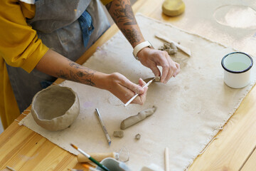 Cropped shot of woman working with clay in pottery studio during masterclass, learning basic...