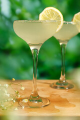 Two drinking glasses of Margarita cocktails with lime and salt, green summer trees on background. Summer alcoholic cocktails. Selective focus.