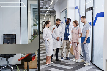 Confident chief medical officer in lab coat pointing at one of healthcare workers during discussion...