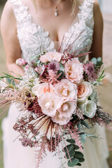 Braut hält ihren Brautstrauß in den Händen mit rosafarbenen Blumen vertikal