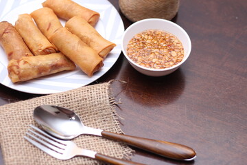 Fried spring rolls with vegetables and tomatoes placed in a black plate on a white wooden table and dipping sauce.