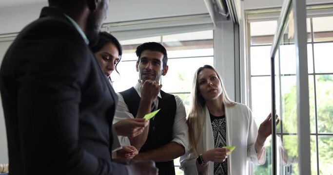 Group of business people tracking tasks on kanban board. Using task control of agile development methodology. Businessman and businesswoman attaching sticky note to scrum task board in the office