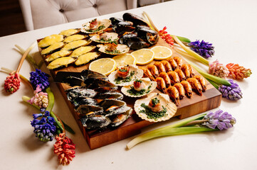 Fried and baked mussels in shells and baked scallops in shell with bacon and sliced lemon on wooden cutting board with card and jacinths