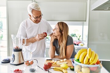 Middle age hispanic couple smiling happy cooking smoothie at the kitchen.