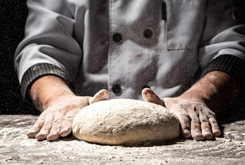 Beautiful and strong men's hands knead the dough from which they will then make bread, pasta or pizza. A cloud of flour flies around like dust. Food concept.