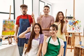 Group of five hispanic artists at art studio pointing finger up with successful idea. exited and happy. number one.