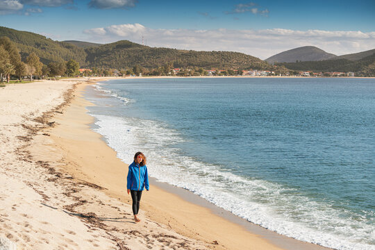A woman in a jacket walks along the autumn resort beach with a fresh breeze from the sea.