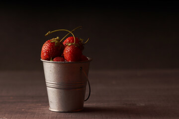 ripe red farm fresh strawberries in a small metal bucket on a dark wooden background